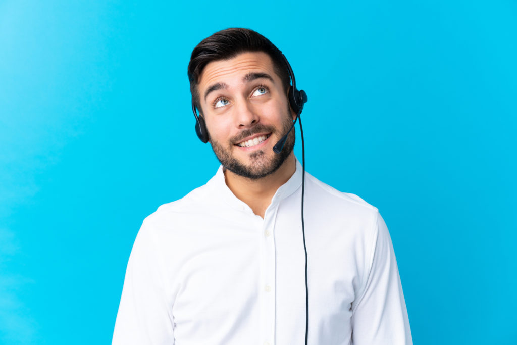 Telemarketer man working with a headset over isolated blue background laughing and looking up